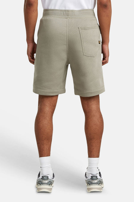 Grijze sweat short van G-Star RAW, achteraanzicht met opgestikte achterzak en merklabel, gedragen met witte sokken en sneakers.