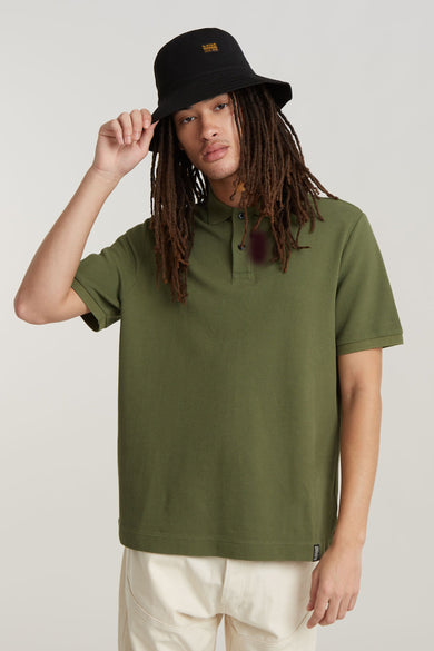 Polo vert de manches courtes G-Star RAW, porté avec un chapeau bucket noir et une légère..