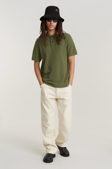 Polo vert de man mantes cour G G G RAW-Star, porté avec un avec bucket hat, des lunettes de soleil et un pantalon beige.