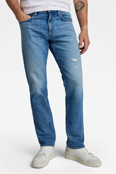 Blauwe denim straight jeans van G-Star RAW, met een kleine scheur op het bovenbeen en witte sneakers.
