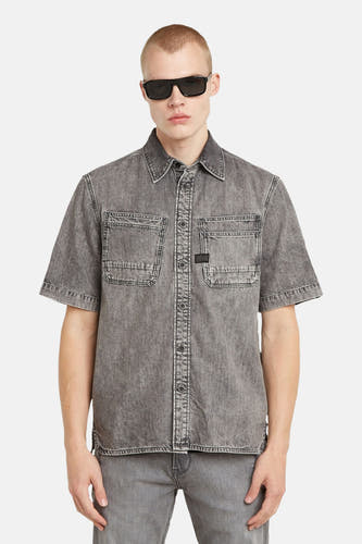 Grijs denim jeanshemd van G-Star RAW, met korte mouwen en twee borstzakken, gedragen met een bijpassende jeans en zwarte zonnebril.