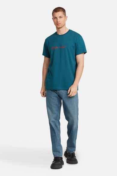 Blauw T-shirt met korte mouwen van G-Star RAW, gedragen met jeans en zwarte schoenen.
