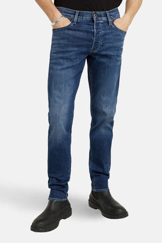 Jeans slim de couleur bleu denim de G-Star RAW, vue de dos, avec des chaussures foncées et un bracelet argenté.