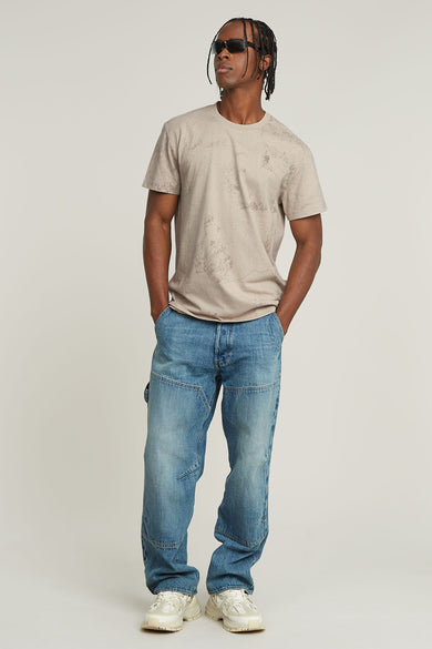 T-shirt beige à manches courtes de G-Star RAW, avec un motif subtil all-over, porté avec un jeans bleu et des baskets blanches.