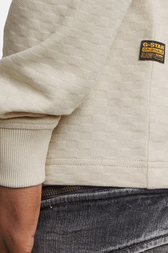 Ecru sweater van G-Star RAW, met geribbelde manchetten en een geweven textuur, gecombineerd met een grijze jeans.
