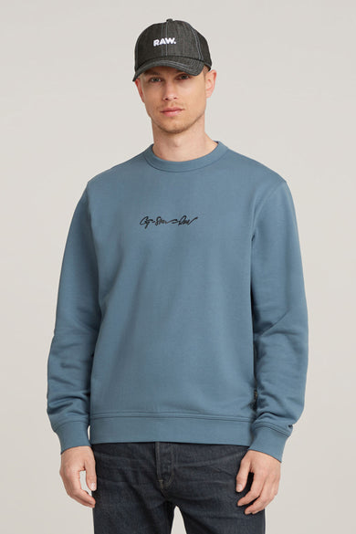 Blauwe sweater met ronde hals van G-Star RAW, met een klein logo op de borst en donkere jeans.
