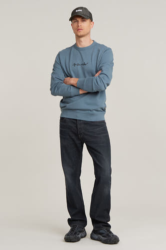 Blauw sweatshirt van G-Star RAW, met gekruiste armen, gecombineerd met donkere jeans en zwarte sneakers.