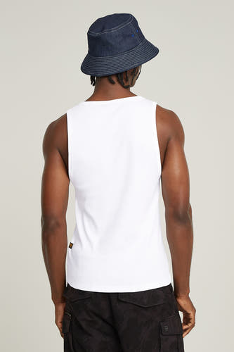 Witte singlet van G-Star RAW, gezien vanaf de achterkant, met een denim bucket hat en camouflage shorts.
