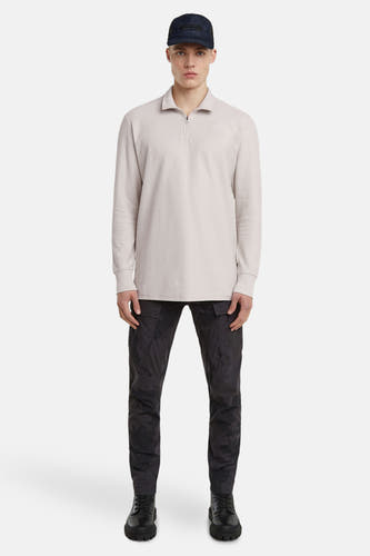 Ecru sweater van G-Star RAW, met lange mouwen, gedragen met een zwarte broek met camouflagepatroon en een pet.