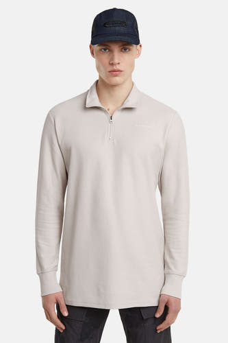 Ecru sweater van G-Star RAW met een kraag met rits en lange mouwen, gedragen met een donkerblauwe pet.
