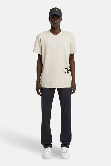 Ecru T-shirt met korte mouwen van G-Star RAW, met een zwarte print en gedragen met een donkere broek en witte sneakers.
