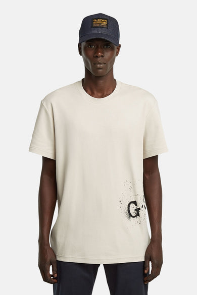 Ecru T-shirt met korte mouwen van G-Star RAW, met een print aan de onderkant en gedragen met een donkerblauwe pet.