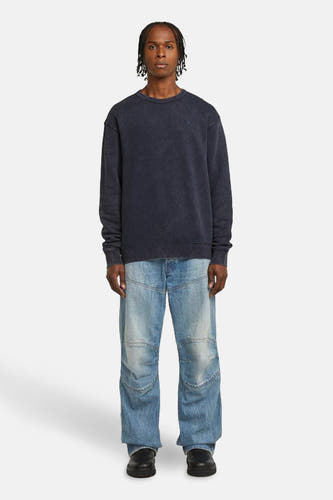 Blauwe sweater met ronde hals van G-Star RAW, gedragen met een wijde, lichtblauwe jeans en zwarte schoenen.

