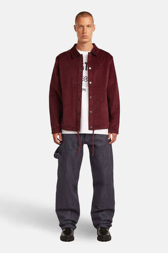 Rode jas van G-Star RAW, met knoopsluiting en losse pasvorm, gecombineerd met een wit T-shirt en wijde, donkere broek.