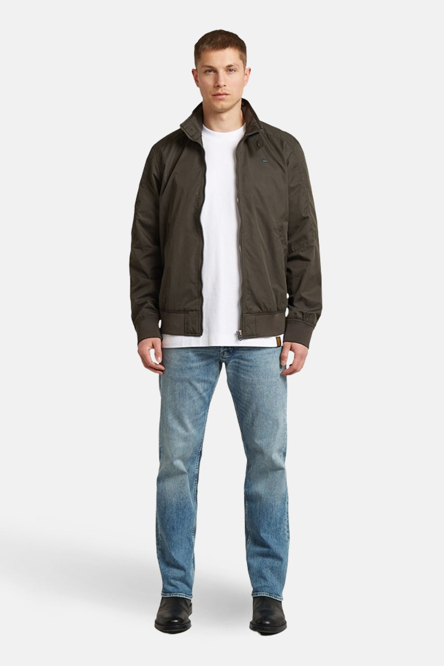 Jean fuselé en denim bleu moyen de G-Star RAW, combiné avec un t-shirt blanc, une veste marron foncé et des chaussures noires.