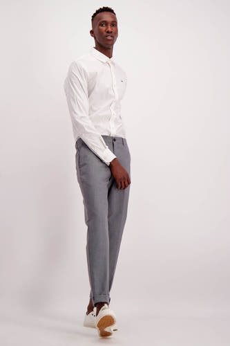 Wit overhemd met lange mouwen van TOMMY JEANS, met knoopsluiting, gedragen met grijze pantalon en witte sneakers.
