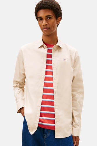 Beige overhemd met lange mouwen van TOMMY JEANS, gedragen over een gestreept T-shirt en een donkerblauwe broek.