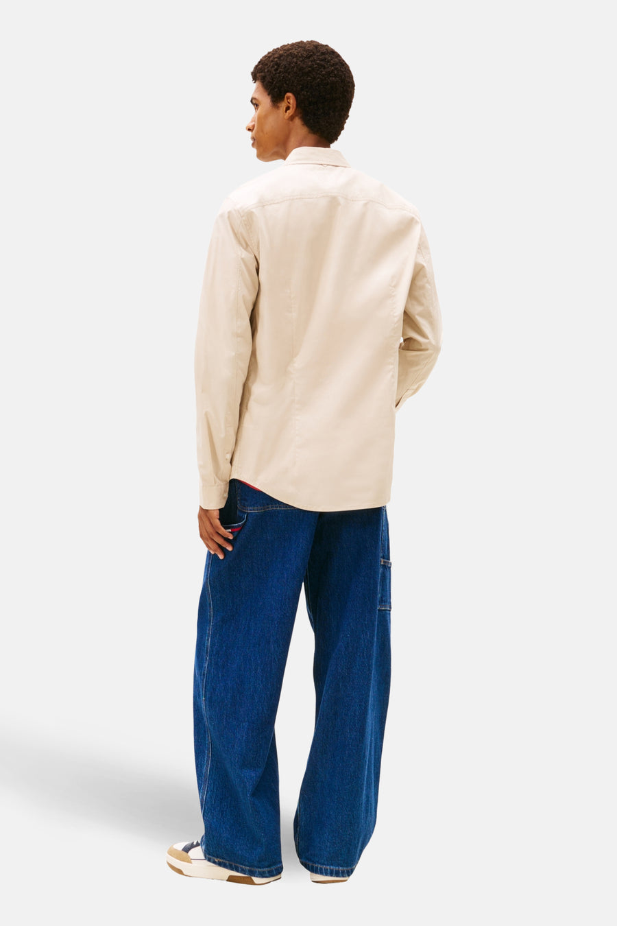Achterkant van een man in een beige overhemd en wijde blauwe jeans.