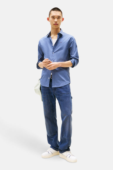 Blauw overhemd met lange mouwen van TOMMY JEANS, met een open kraag en geknoopte manchetten, gedragen over een wit shirt.
