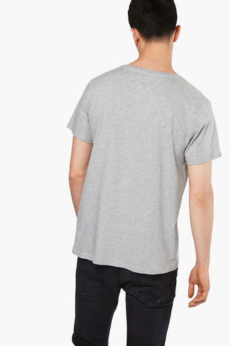 Grijs T-shirt van TOMMY JEANS, rugzijde gezien, gecombineerd met zwarte jeans.