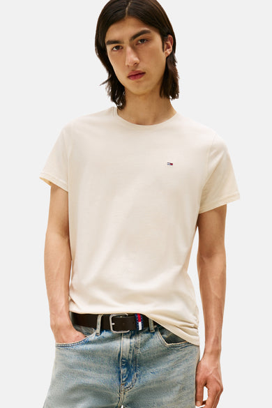 Beige T-shirt met korte mouwen van TOMMY JEANS, gedragen met blauwe jeans en een zwarte riem.
