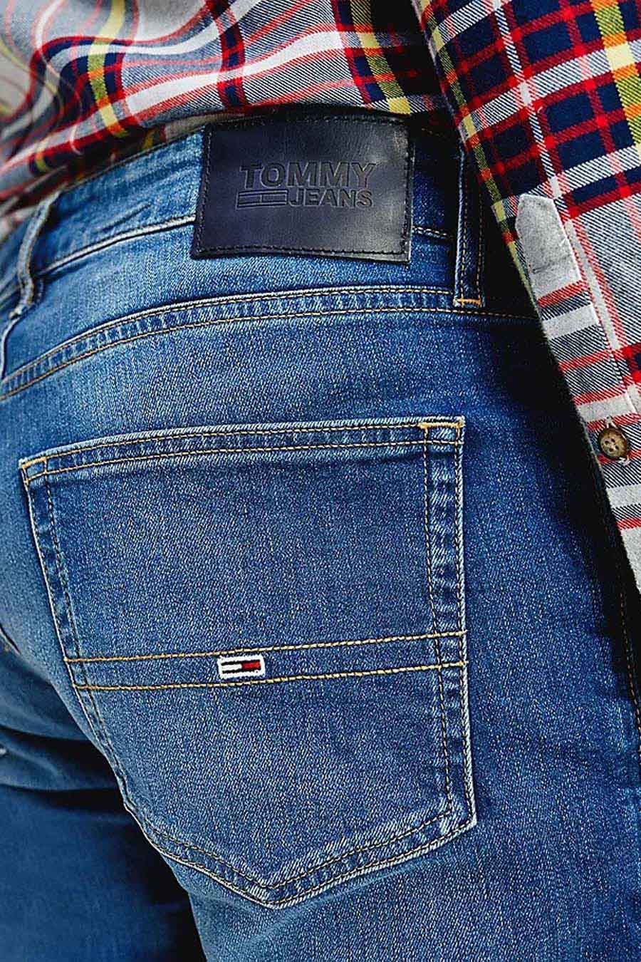 Blauwe rechte jeans van TOMMY JEANS, met achterzak en leren merklabel, gecombineerd met geruit overhemd.
