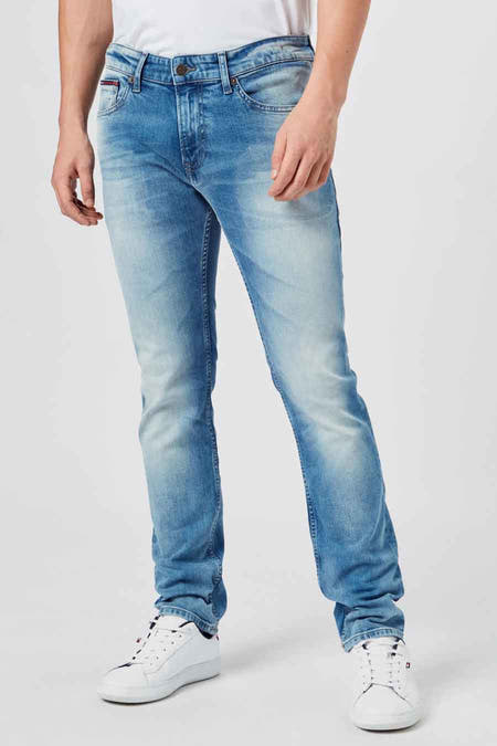 Lichtblauwe slim-fit jeans van TOMMY JEANS met verbleekt effect, zichtbare naadwerk en klassieke vijfzakkenstijl, gedragen met witte sneakers.