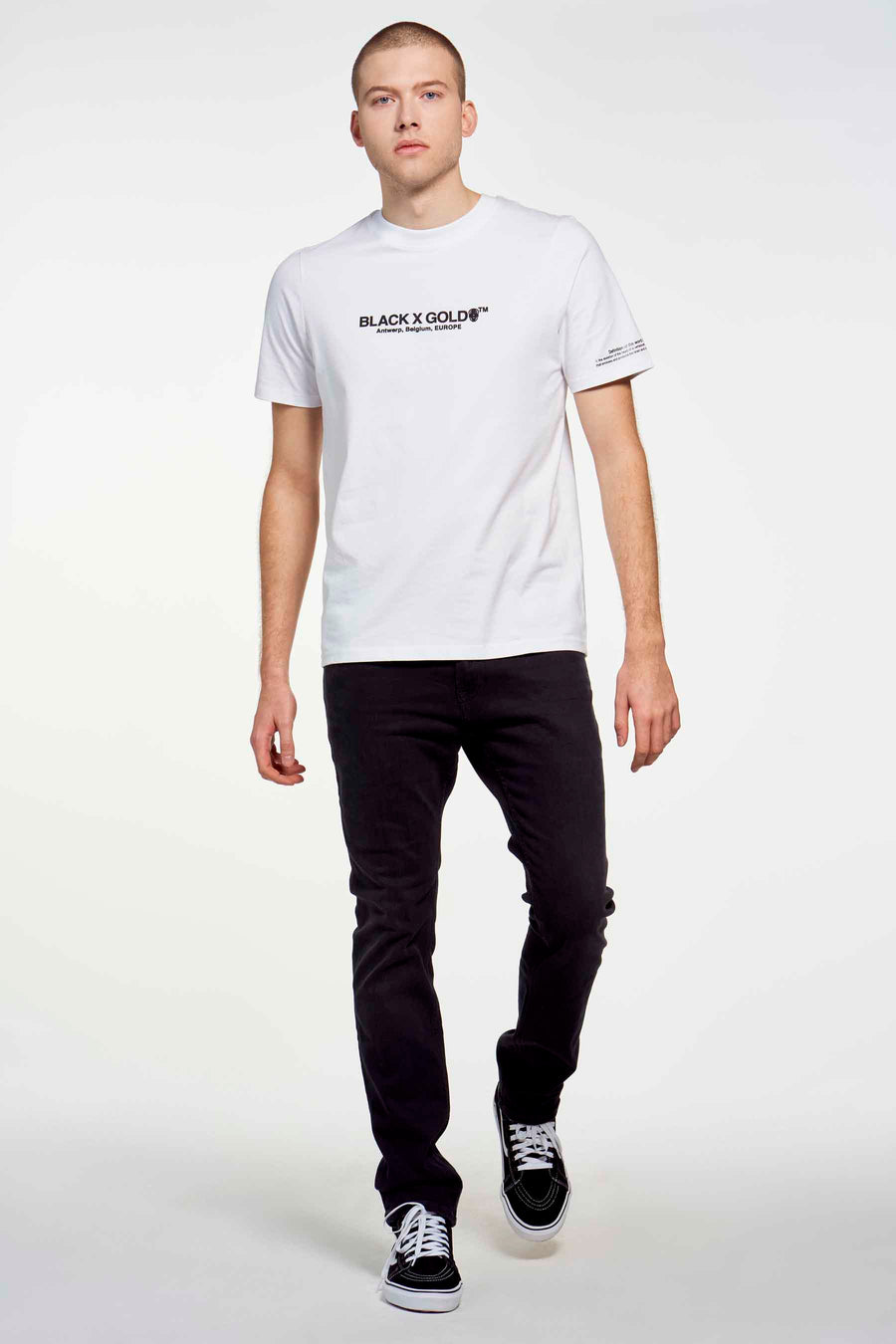 Donkergrijze slim jeans van TOMMY JEANS, gecombineerd met een wit T-shirt en zwarte lage sneakers.