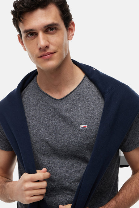 Grijs mêlee T-shirt van Tommy Jeans met V-hals, klein logo op de borst en een marineblauwe trui over de schouders.