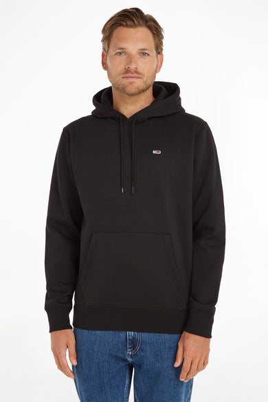 Zwarte hoodie met capuchon van TOMMY JEANS, voorzien van kleine logo op borst en voorzak, gedragen door man in blauwe jeans, front view.