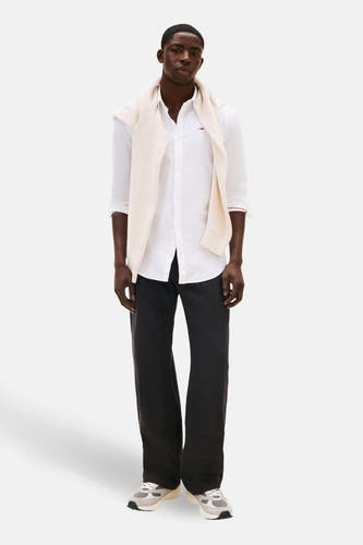 Wit overhemd met lange mouwen van TOMMY JEANS, gedragen met een vest over de schouders en een zwarte broek.
