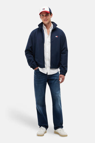 Wit hemd met lange mouwen van TOMMY JEANS, gedragen onder een navyblauwe jas, jeans en een pet.