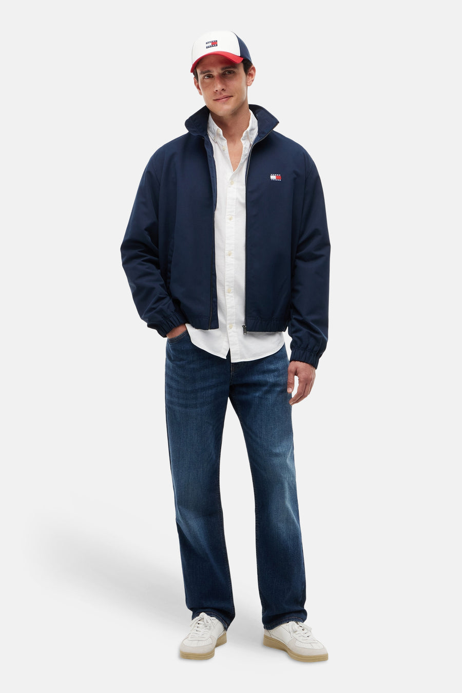 Wit hemd met lange mouwen van TOMMY JEANS, gedragen onder een navyblauwe jas, jeans en een pet.
