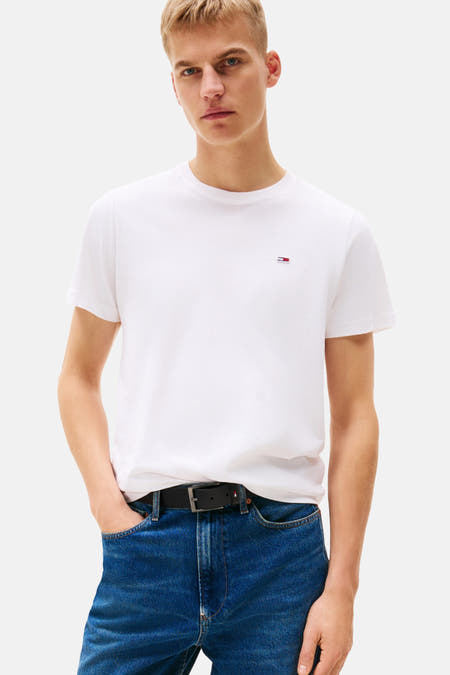 Wit T-shirt met korte mouwen van Tommy Jeans, gedragen met blauwe jeans en een zwarte riem.
