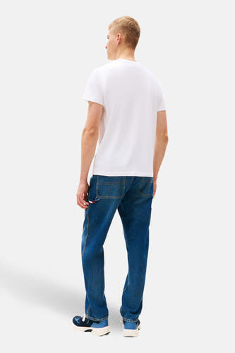 T-shirt blanc à manches courtes de Tommy Jeans, vu de derrière, associé à des jeans bleus et des baskets.