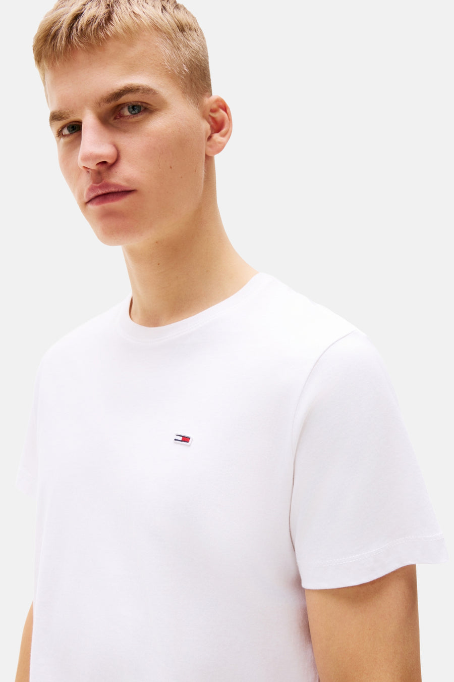 T-shirt blanc à manches courtes et col en V de TOMMY JEANS, avec petit logo drapeau sur la poitrine et étiquette de marque dans le cou.