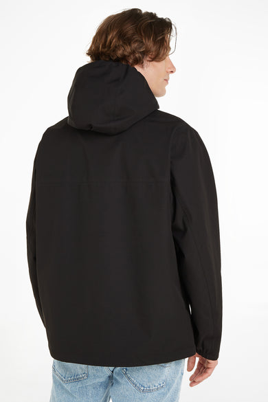 Zwarte korte jas met capuchon van TOMMY JEANS, achterzijde weergegeven, gladde stof, model draagt lichtblauwe jeans