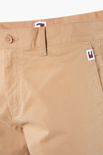 Beige short van TOMMY JEANS, detailopname van de tailleband met knoop en logo op de zak.
