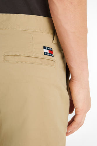 Beige short van TOMMY JEANS, met achterzak en logopatch, tegen een witte achtergrond.
