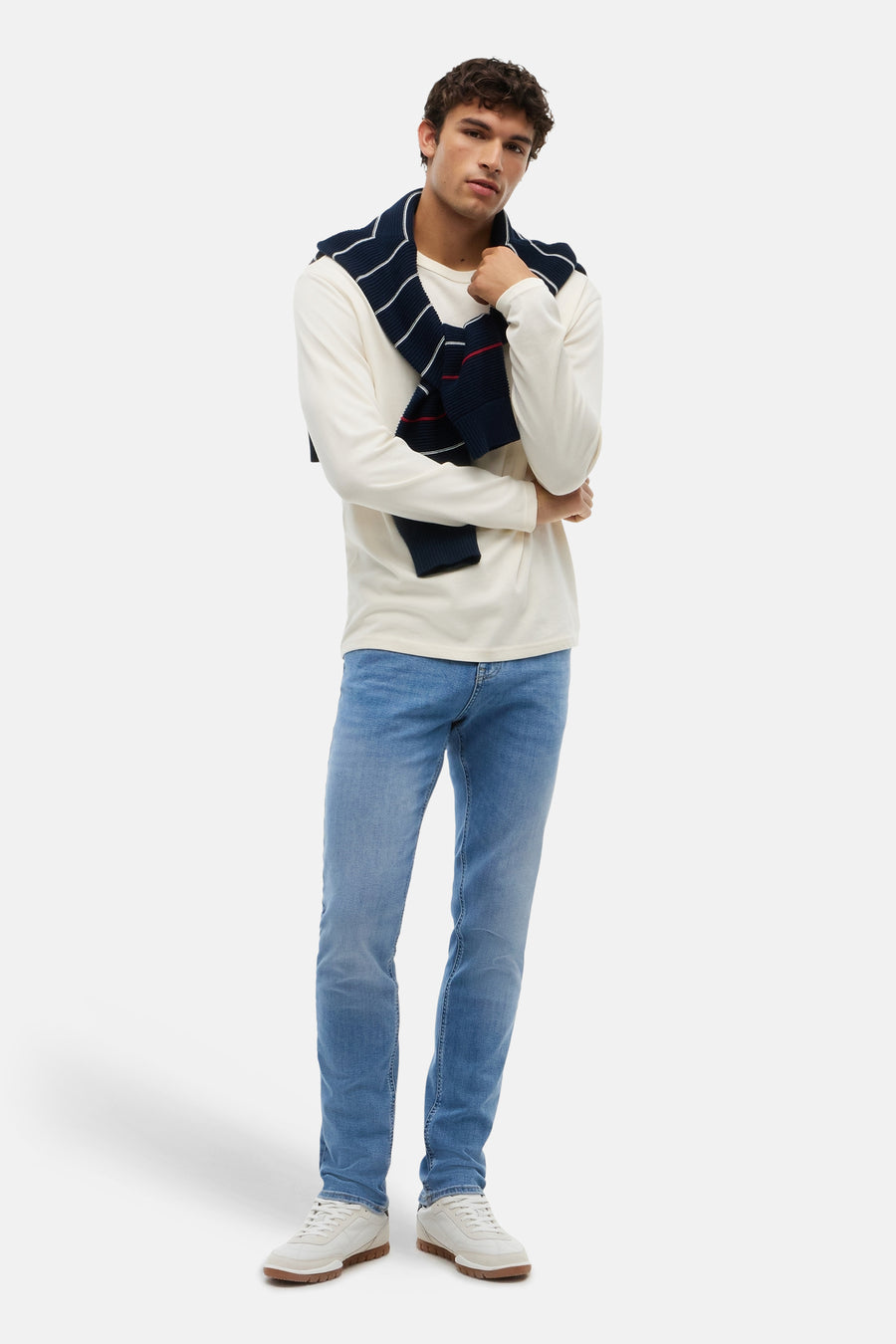 Jean slim bleu moyen de TOMMY JEANS, porté avec un pull blanc et une écharpe tricotée, visage lifestyle, en pied.