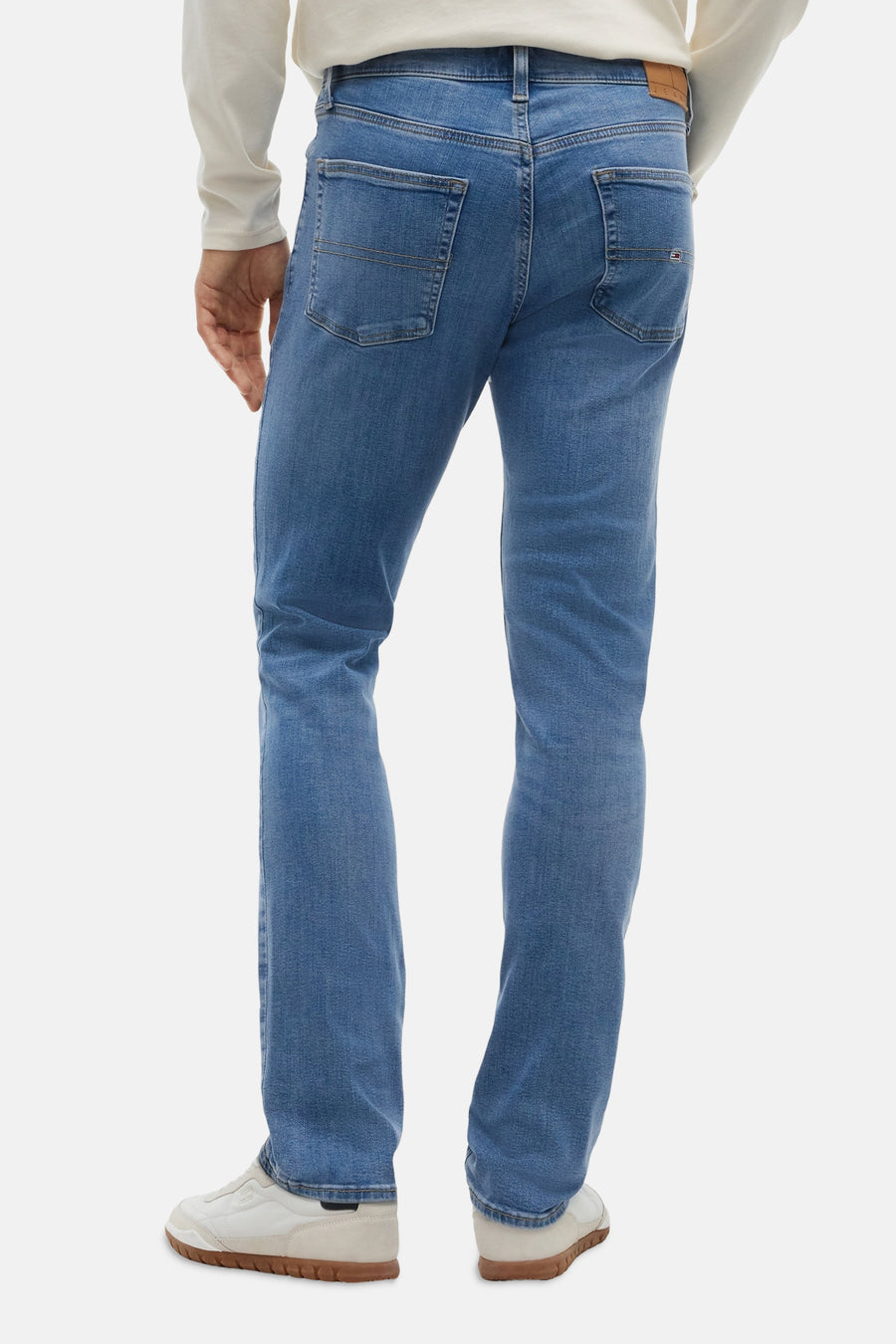 Jean slim bleu moyen de TOMMY JEANS, dos avec poches et légère décoloration, porté avec un pull blanc et des baskets