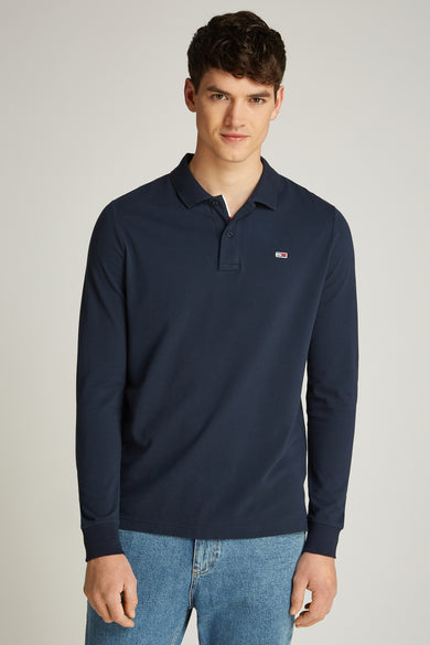 Blauw poloshirt met lange mouwen van TOMMY JEANS, met een klein logo op de borst, gedragen met jeans.
