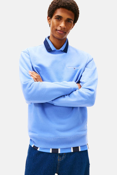 Blauwe sweater van TOMMY JEANS, met lange mouwen en ronde hals, gedragen over een gestreept shirt.