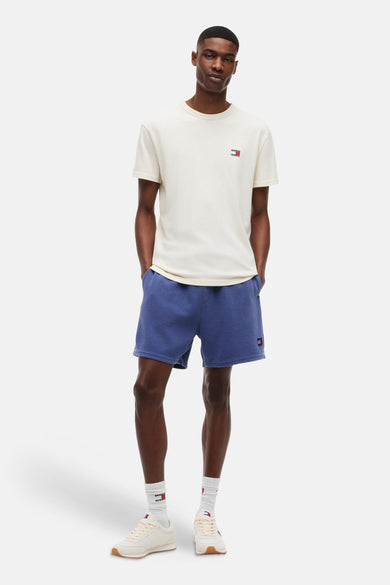Crèmekleurig T-shirt met korte mouwen van TOMMY JEANS, met klein logo op de borst, gedragen door een man met blauwe shorts.