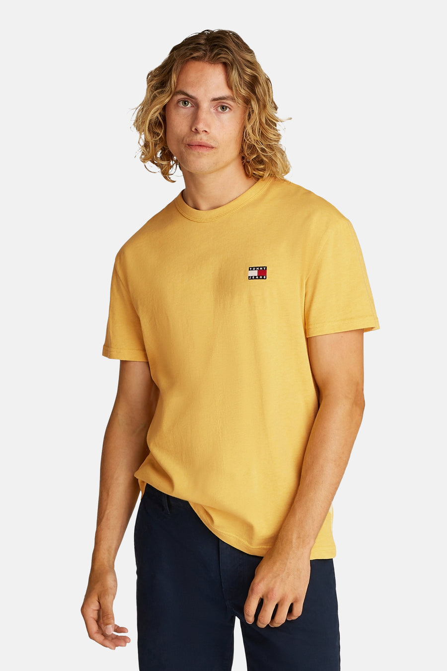 T-shirt jaune à manches courtes de TOMMY JEANS, vu de dos, avec des shorts bleus marine, des chaussettes blanches et des baskets.