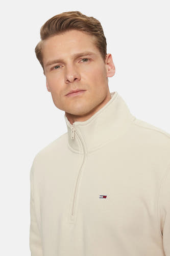 Beige ronde hals sweater van TOMMY JEANS met halve rits en klein logo op borst, close-up van model