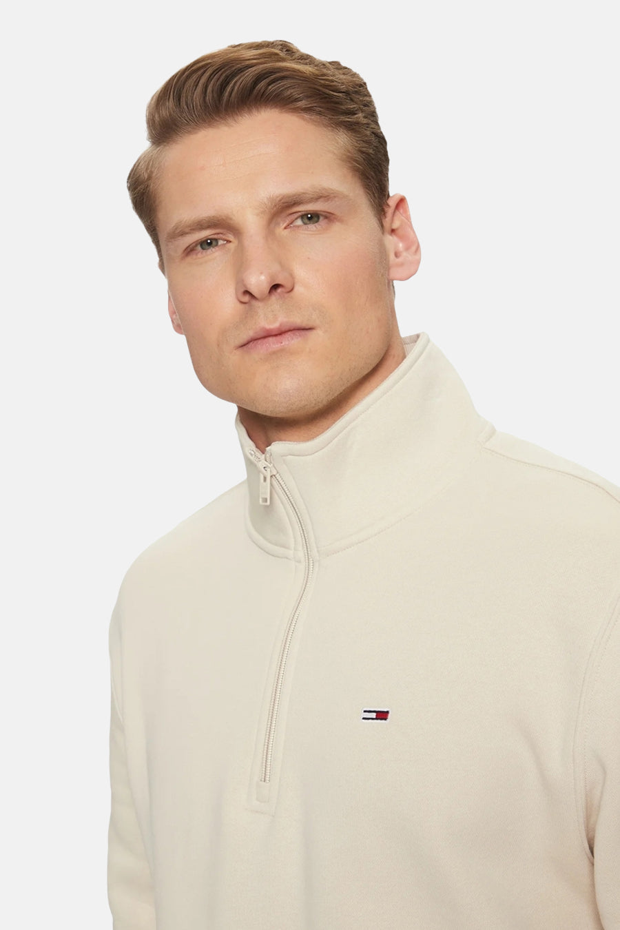 Beige ronde hals sweater van TOMMY JEANS met halve rits en klein logo op borst, close-up van model