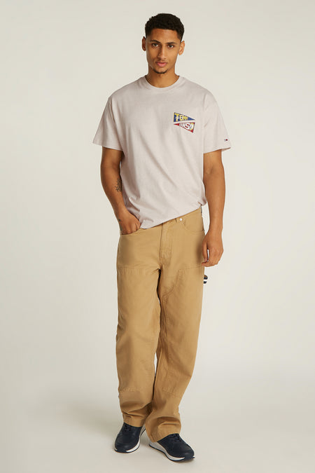 Ecru T-shirt met korte mouwen van TOMMY JEANS, met een logo op de borst en gedragen met bruine broek en blauwe sneakers.
