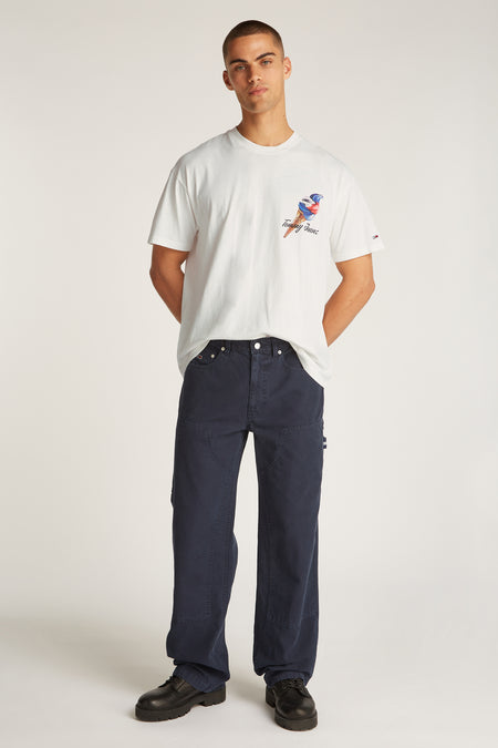 Wit T-shirt met korte mouwen van TOMMY JEANS, met een print van een ijsje, gecombineerd met een donkerblauwe broek en zwarte schoenen.
