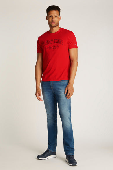 T-shirt rouge à manches courtes de TOMMY JEANS, avec une impression sur la poitrine et associé à des jeans et des baskets.